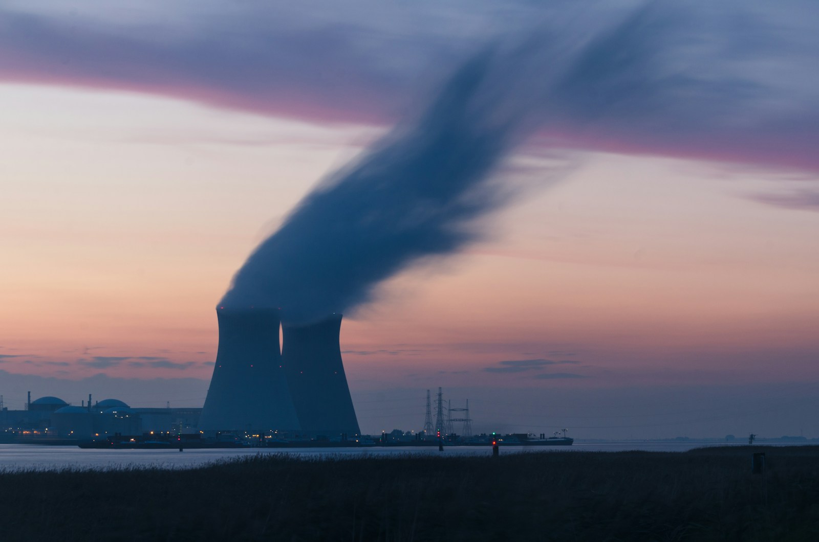 photography of nuclear energy cooling tower blowing smokes under white and orange sky at daytime